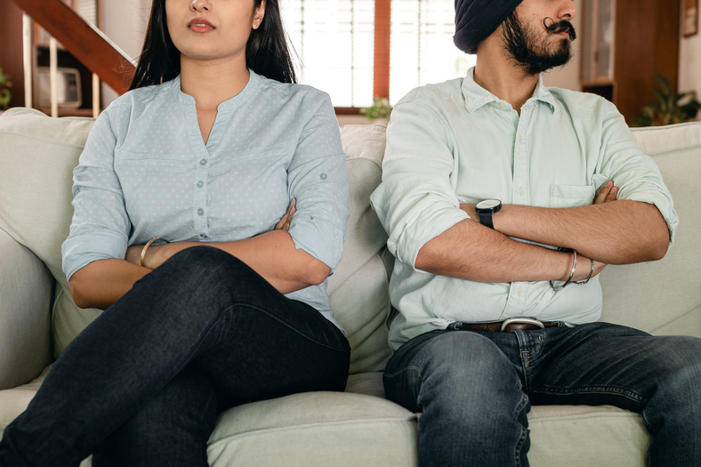 Anonymous ethnic couple sitting on sofa having marriage issues